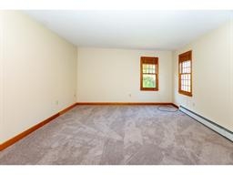 Empty room with beige walls, carpeted floor, and two windows with wooden trim.