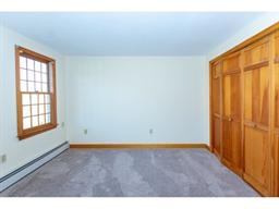 Empty bedroom with a window, beige carpet, and wooden closet doors.