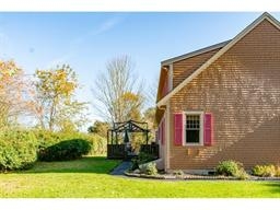 Side view of a house with red shutters and a gazebo in a grassy yard.