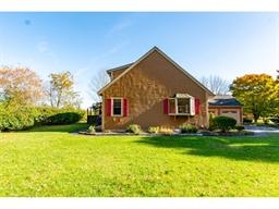 Brown house with red shutters, surrounded by green lawn and trees on a sunny day.