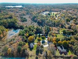 Aerial view of a wooded suburban area with houses, roads, and a small pond.