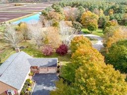 Aerial view of a house, driveway, colorful trees, and a pond in the background.