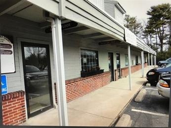 Storefronts with large windows and a covered sidewalk next to a parking lot.