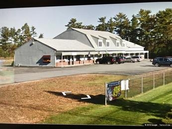 A gray two-story building with parked cars and a fenced grassy area in front.
