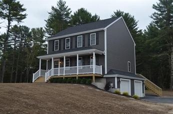 Two-story gray house with white trim, front porch, and attached garage on a sloped lawn.