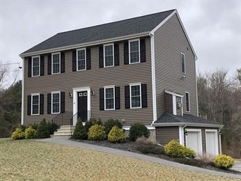 Two-story brown house with black shutters and a double garage on a sloped lawn.