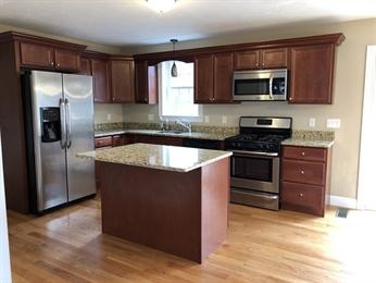 Modern kitchen with wood cabinets, granite island, and stainless steel appliances.