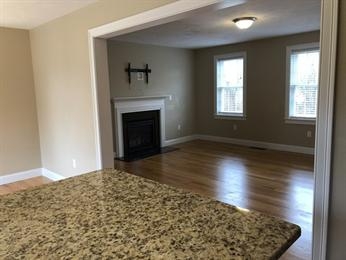 View of a living room with fireplace, hardwood floors, and granite countertop in foreground.
