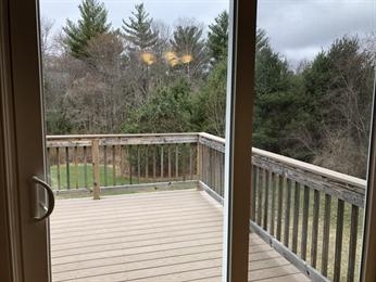 Wooden deck with railing overlooking trees, seen through a glass door on a cloudy day.