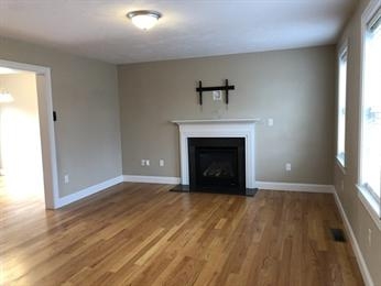 Empty living room with hardwood floors, fireplace, and large windows letting in natural light.