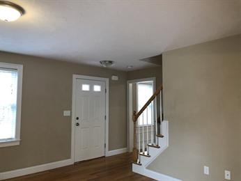 Entryway with white front door, beige walls, hardwood floors, and a small staircase.