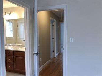 Open doorways reveal a bathroom with a sink and a hallway with wooden floors and white walls.