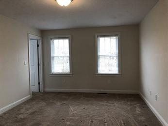 Empty room with beige walls, two windows, carpeted floor, and a door to the left.