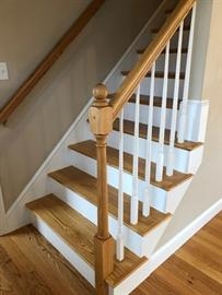 Wooden staircase with white risers, wooden handrail, and white vertical balusters.