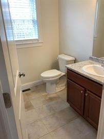 Small bathroom with a toilet, sink cabinet, and a window with blinds.