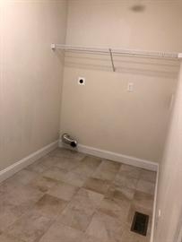 Empty laundry room with tile floor, wall vent, and a single wire shelf.