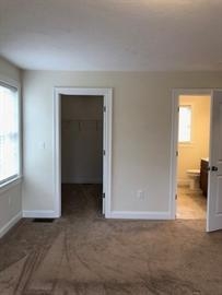 Bedroom with beige carpet, two doorways to a closet and a bathroom, and a window.