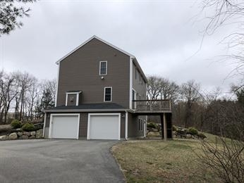 Two-story gray house with double garage, a deck, and a driveway on a cloudy day.