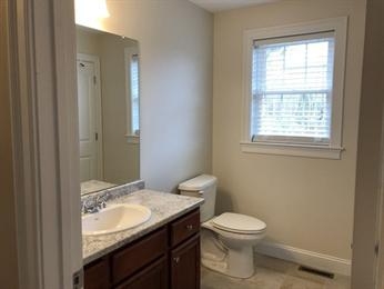 Small bathroom with a vanity, sink, toilet, mirror, and a window with blinds.