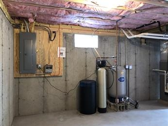Unfinished basement with utility equipment, electrical panel, and exposed insulation.