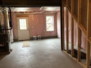 Unfinished basement with exposed insulation, concrete floor, and a door with a window.