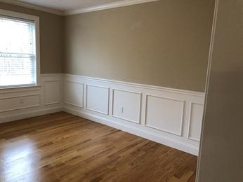 Empty room with light wood floor, beige upper walls, white wainscoting, and a window.