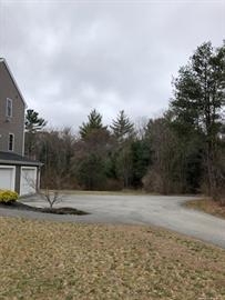 Gray house with a three-car garage next to a curved driveway and trees under cloudy skies.