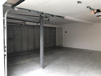 Empty two-car garage with concrete floor, central support beam, and a closed back door.