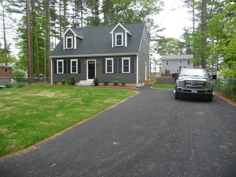 Gray house with black shutters and a long driveway, a truck parked near the house.