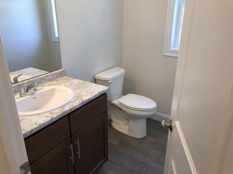 Small bathroom with a sink, mirror, toilet, window, and light gray flooring.