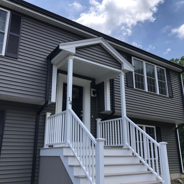 Gray house with black shutters, white steps and railing, and a covered entryway.