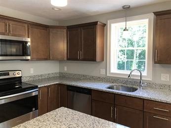 Modern kitchen with brown cabinets, granite countertops, and stainless steel appliances.
