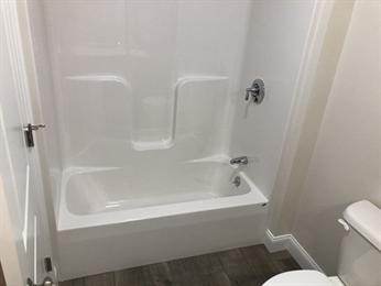 White bathtub and shower with chrome fixtures next to a toilet in a small bathroom.