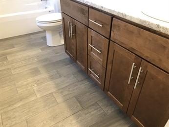 Bathroom with wood cabinets, gray tile floor, and a toilet next to a white bathtub.
