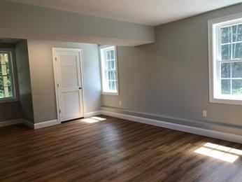 Empty room with wood flooring, gray walls, white trim, and two windows letting in sunlight.