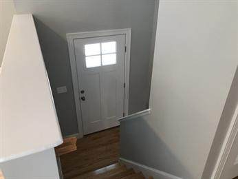View of a white front door with window panes at the bottom of a staircase in a home.