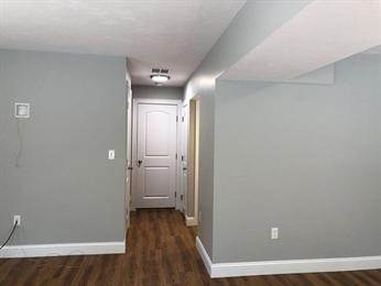 Hallway with gray walls, white door, and wood flooring, under ceiling light.