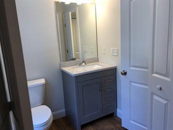 Small bathroom with a gray vanity, sink, mirror, toilet, and white walls.