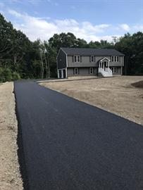 A newly paved driveway leading to a gray two-story house with white stairs.