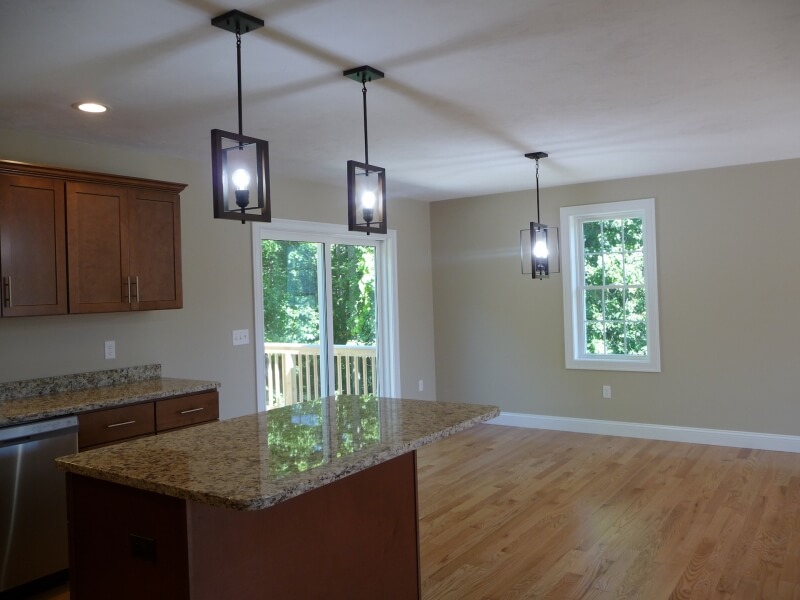 Modern kitchen with granite island, wood cabinets, pendant lights, and hardwood floor.