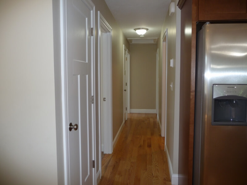 A hallway with wooden floor, white doors, beige walls, and a refrigerator on the right.