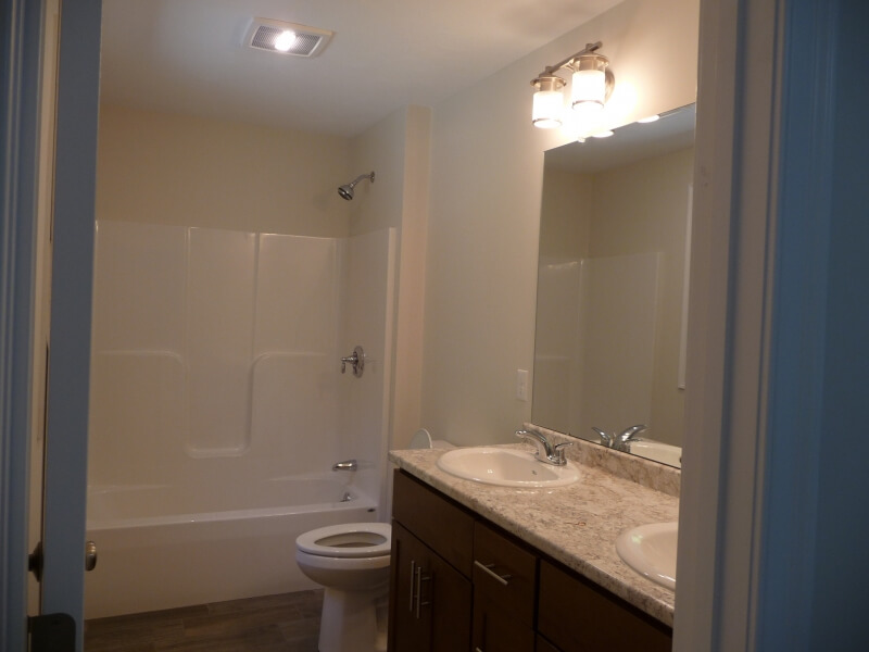 Small bathroom with a bathtub, toilet, double sinks, and a large mirror above the vanity.