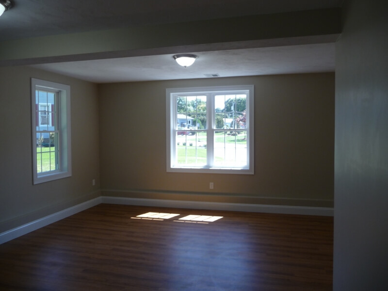 Empty room with tan walls, wood flooring, and two large windows letting in natural light.