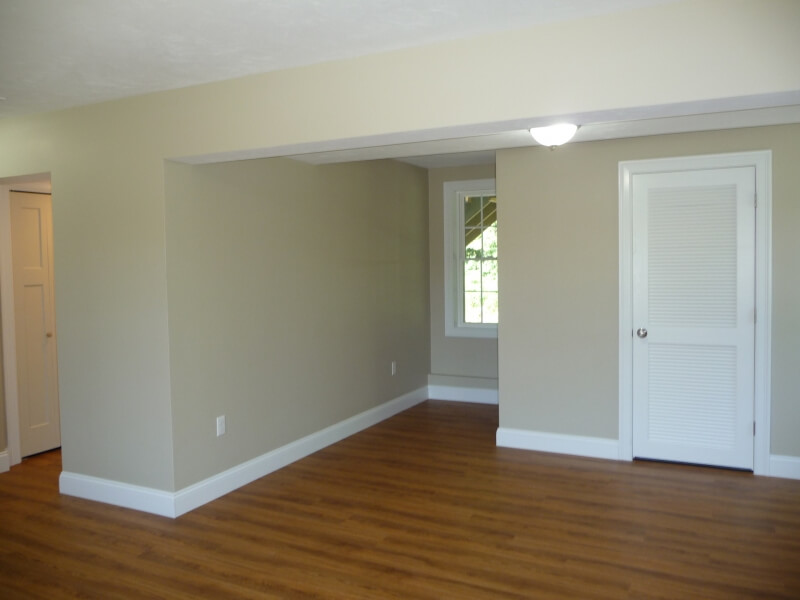 Empty room with light beige walls, wood flooring, a white door, and a window.