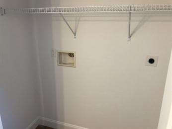 Empty laundry closet with a wire shelf and water hookups on a plain white wall.