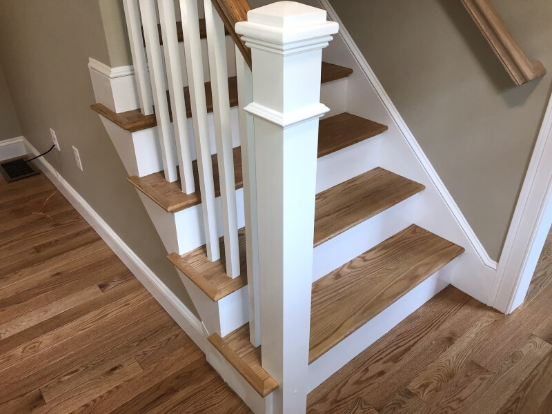 Stairs with wooden steps, white risers, and a white banister against a beige wall.