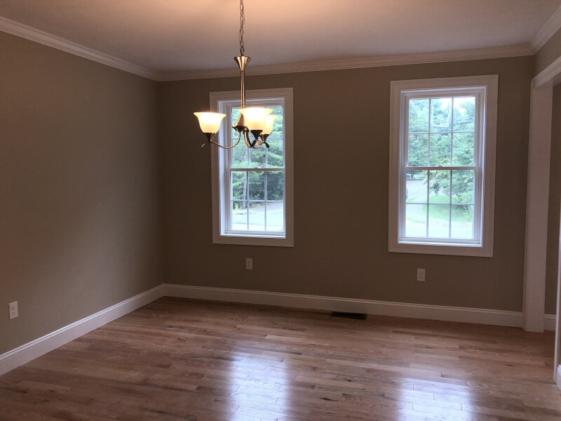 Empty room with wooden floor, beige walls, two windows, and a ceiling light fixture.