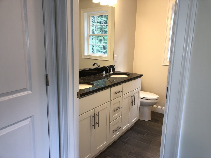 Modern bathroom with double sink vanity, dark countertop, and a toilet near two windows.