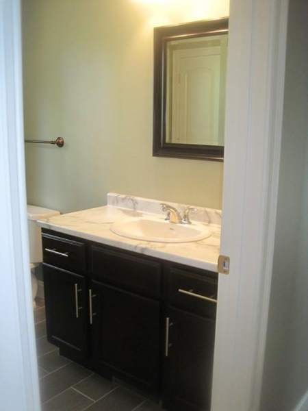 Bathroom with dark cabinets, marble countertop, mirror, and silver faucet, seen from doorway.