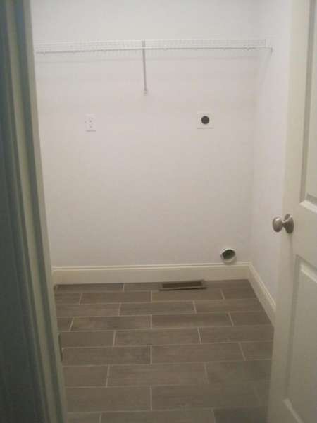 Empty laundry room with tiled floor, white walls, a wire shelf, and utility hookups.